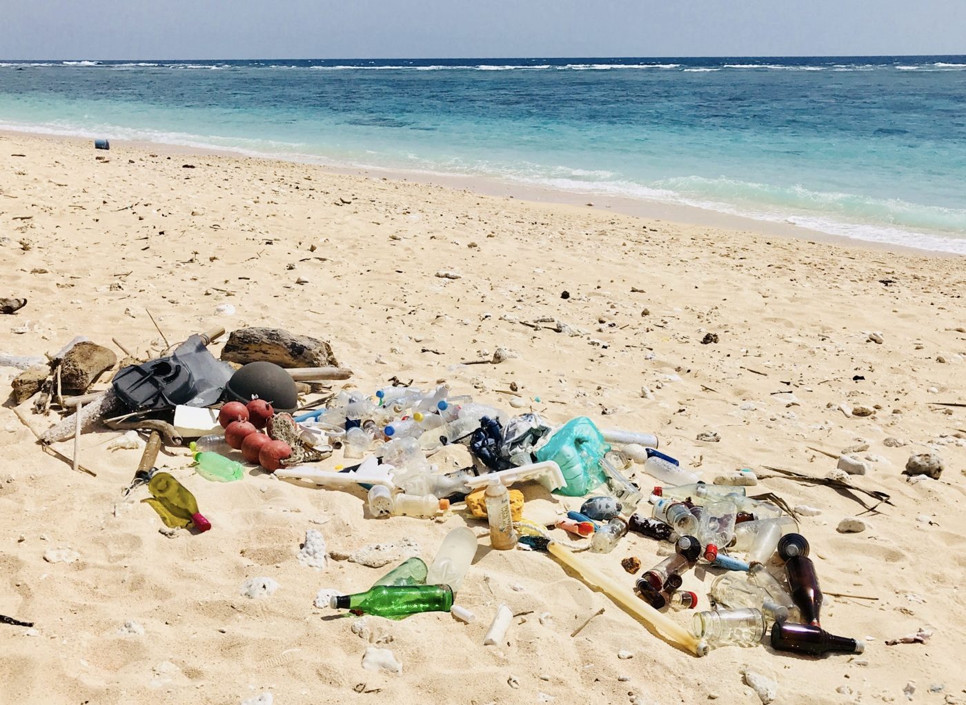 Plastic bottles and debris washed up on a white-sand beach