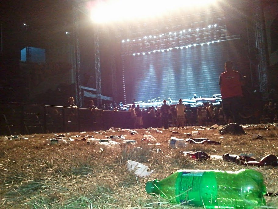 A festival field strewn with bottles and cups in front of the stage